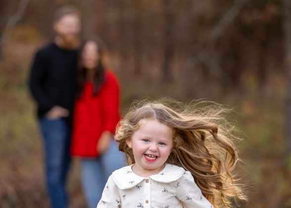 Little girl running with her parents behind her in autumn