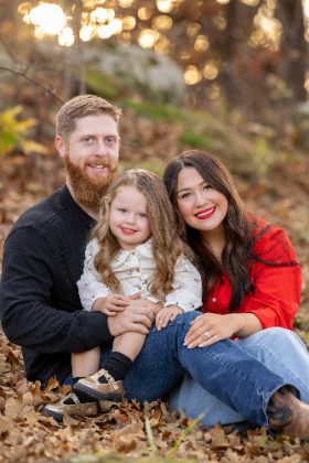 Family of three sitting in fall leaves