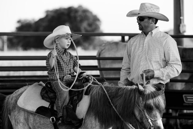 Black and white photo of a father and son with horses at the arena