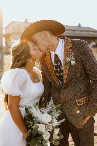 Western couple in cowboy hat sharing a kiss with bouquet