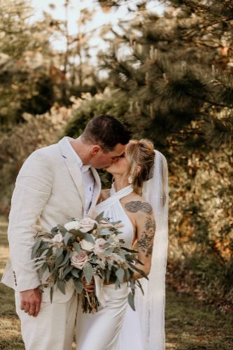 Bride and groom kissing among the trees with greenery bouquet