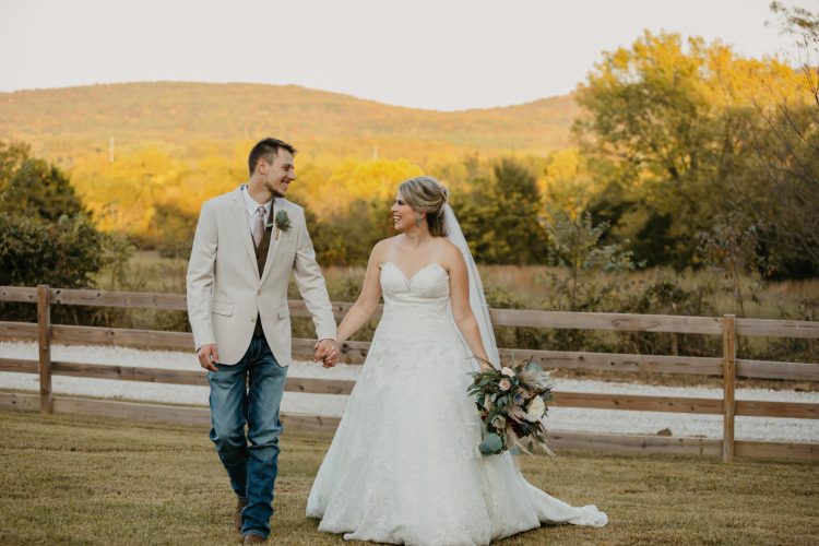 Bride and groom walking along a ranch fence line